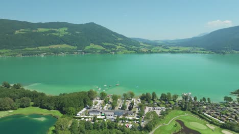 luxurious lakeside: the drone showcases the tranquility of mondsee lake, embraced by the grandeur of austrian mountains, offering a glimpse of a golf resort