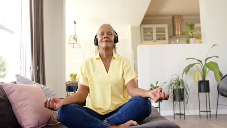 african american senior woman wearing headphones, meditating at home