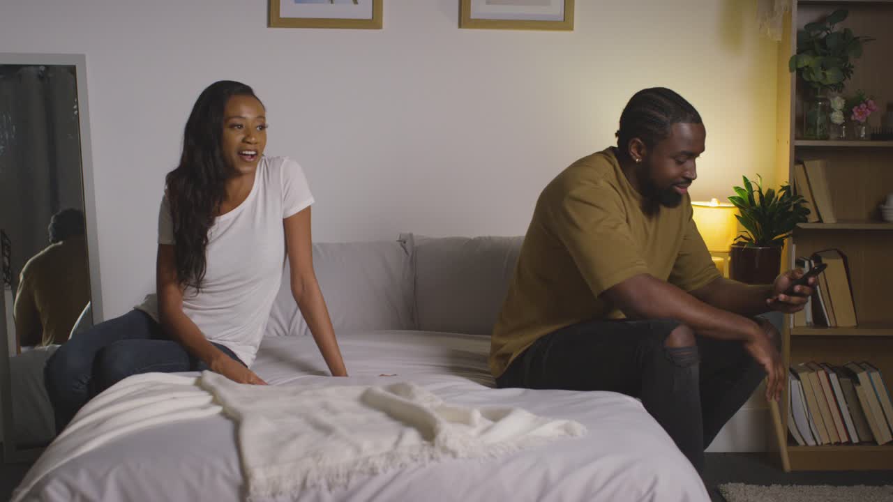 pareja joven en casa por la noche en el dormitorio con una mujer hablando con un hombre desplazándose por internet en el teléfono móvil 3