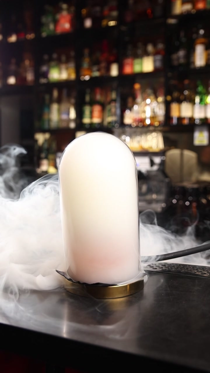 Fumée blanche s'élevant d'une cloche en verre sur un comptoir de bar