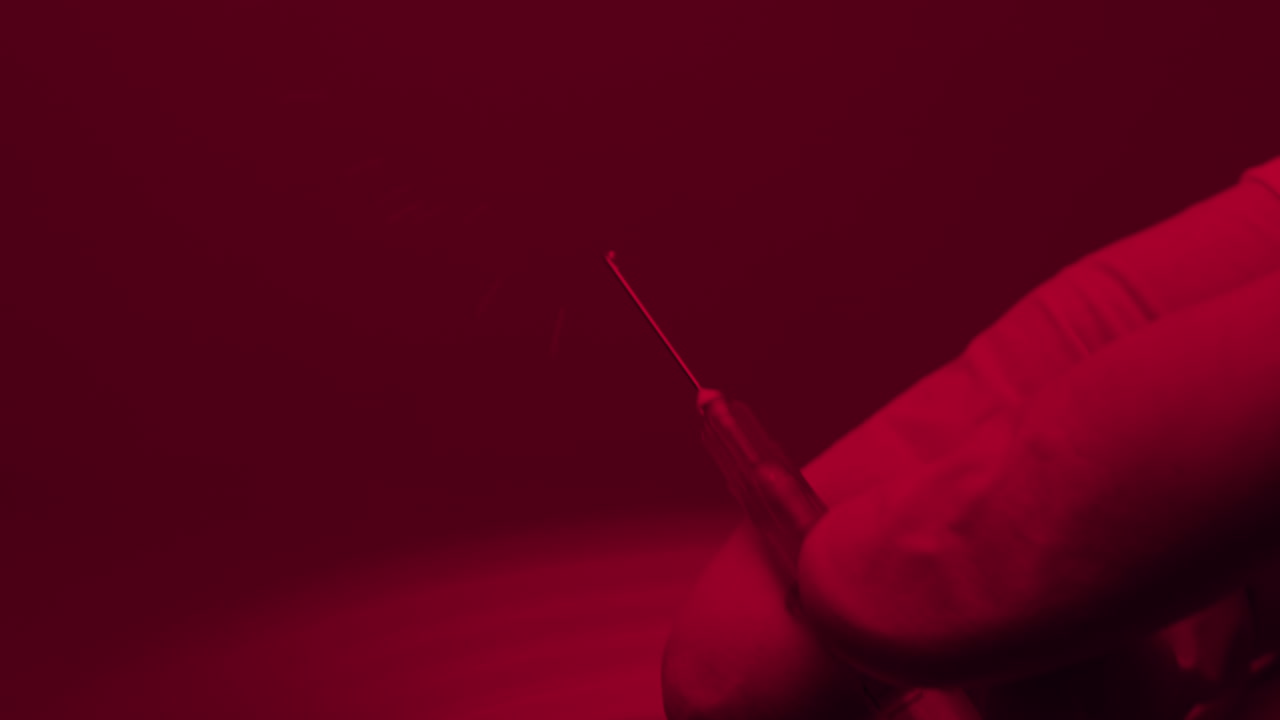 hand in gloves preparing a syringe before the injection , close up in red light emergency room