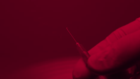 hand in gloves preparing a syringe before the injection , close up in red light emergency room