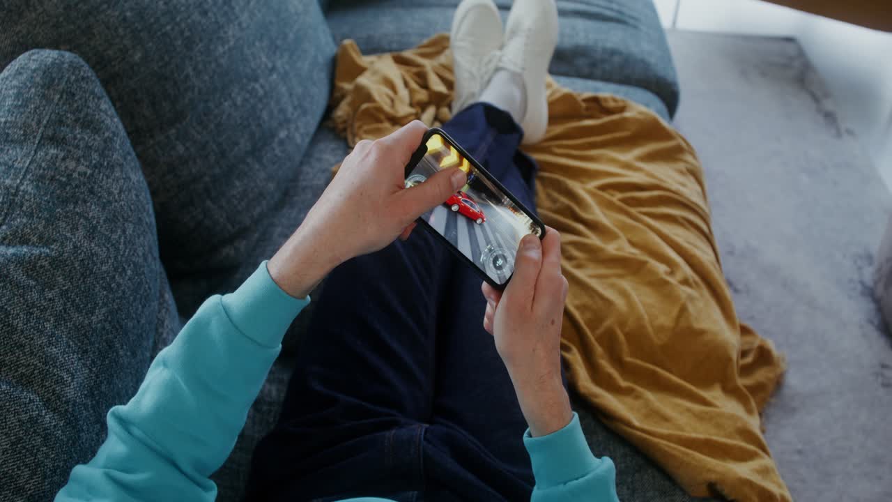 Person playing car racing game on smartphone while relaxing on couch