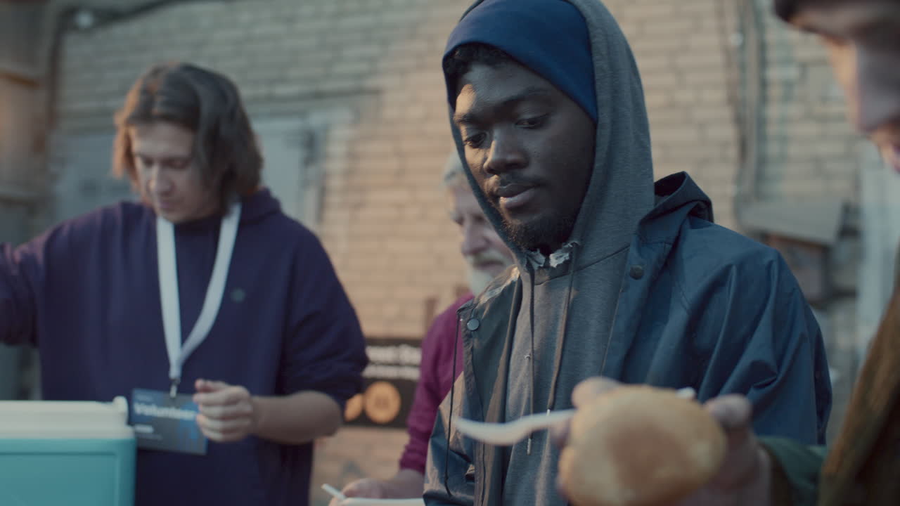 Volunteers Providing Food and Water to Homeless Men in City Alley