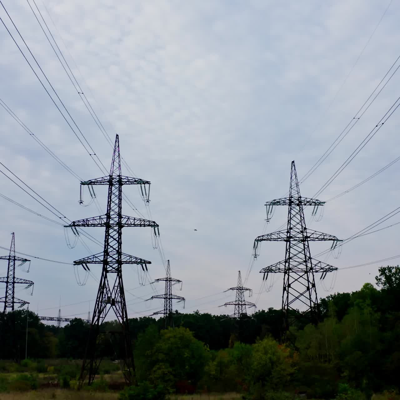 Electricity pylons bearing the power supply across a rural landscape during sunset. Selective focus