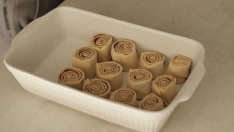 white male chef placing homemade cinammon rolls into white ceramic baking tray