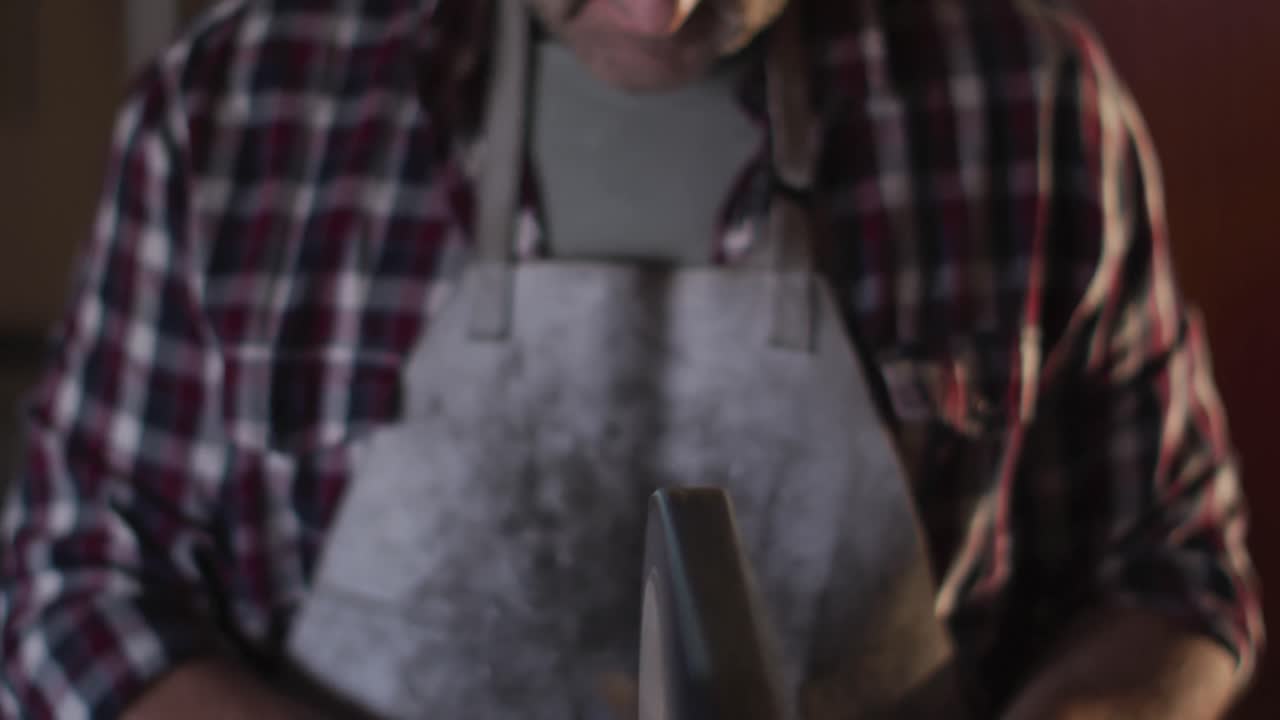 primer plano de un hombre caucásico fabricante de cuchillos en un taller con gafas y usando una lijadora