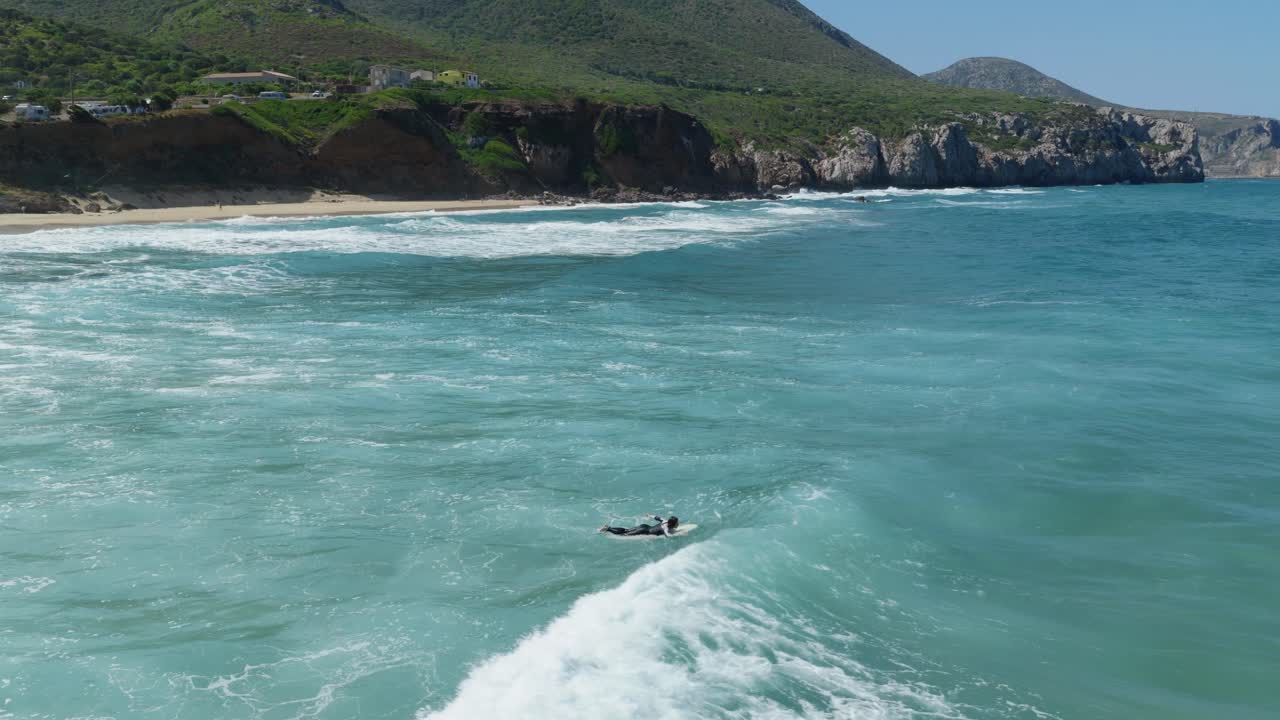 Surfer rides waves on Sardegna's scenic west south coast, tranquility abounds