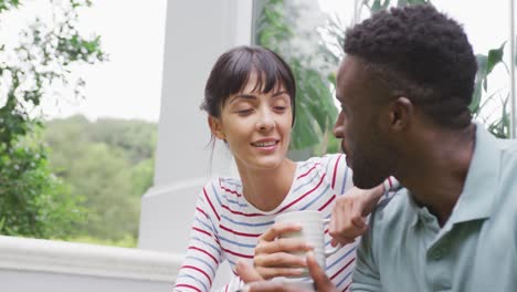 happy diverse couple wearing blouse and shirt talking and drinking coffee in garden