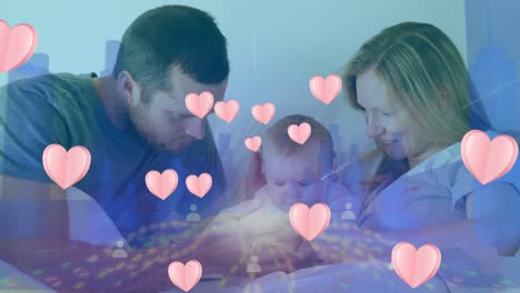 animación de iconos de corazones rosados flotando sobre una pareja caucásica jugando con su bebé en la cama.