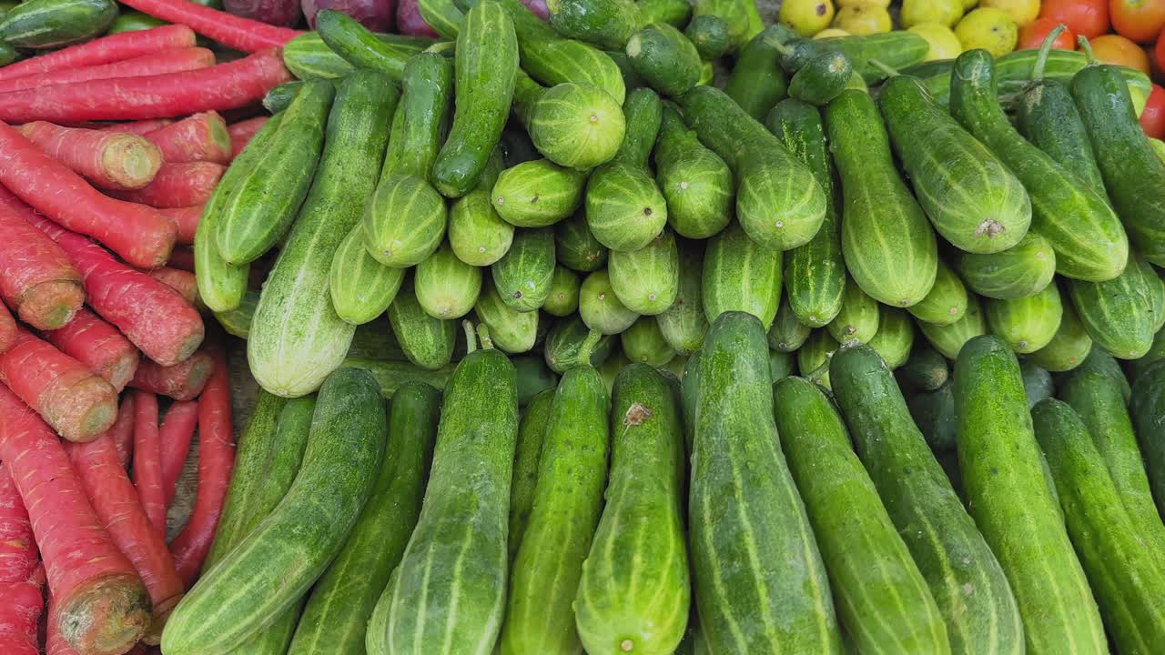 Tracking shot of fresh cucumbers (kheera) stacked in neat piles at an Indian sabzi mandi, showcasing their bright green texture and vibrant market arrangement