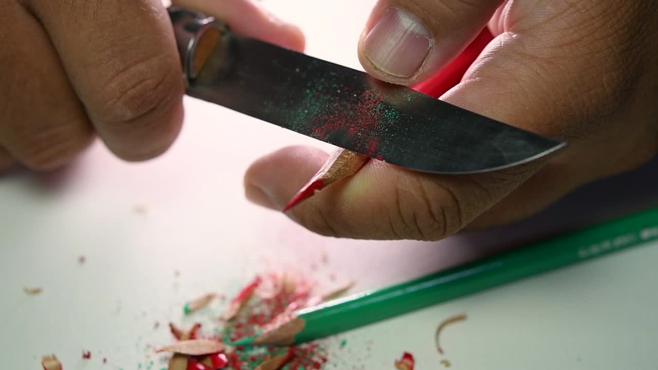 Opptak av hender som sakte spisser en blyant og noen fargeblyanter med en skarp kniv