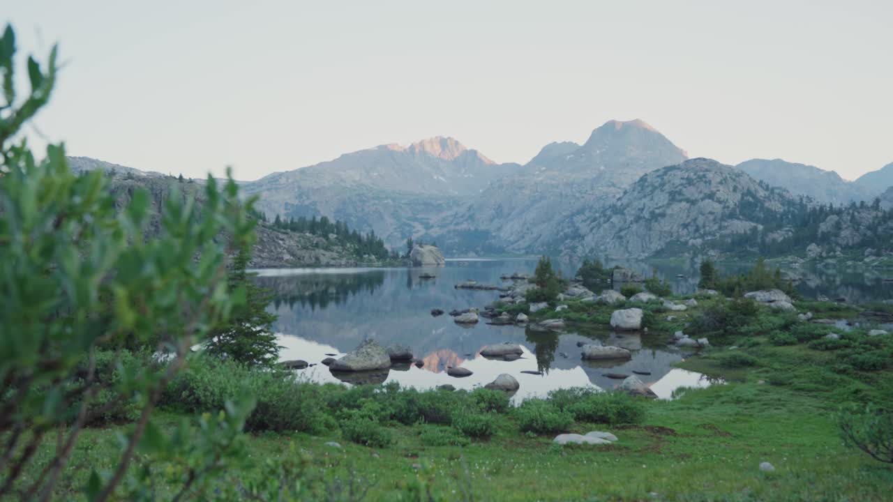 горный ландшафт с спокойным озером, окруженным зеленью в ветре речной цепи на рассвете