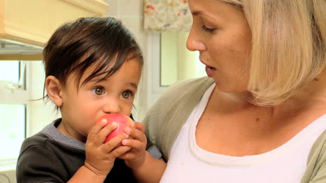 baby in mothers arms eating a red apple