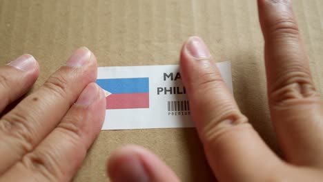 hands applying made in philippines flag label on a shipping box with product premium quality barcode