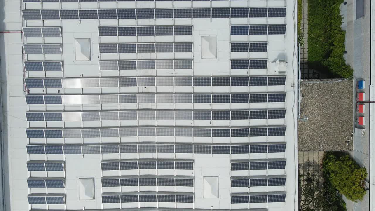 Top down aerial of industrial buildings covered with photovoltaic solar panels. The drone descends to the solar panels
