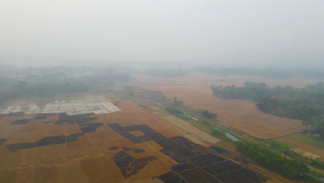 Eine-Vogelperspektive-Auf-Ein-Verbranntes-Ackerland-Nach-Der-Ernte-Neben-Einem-Kanal-Im-Nebel