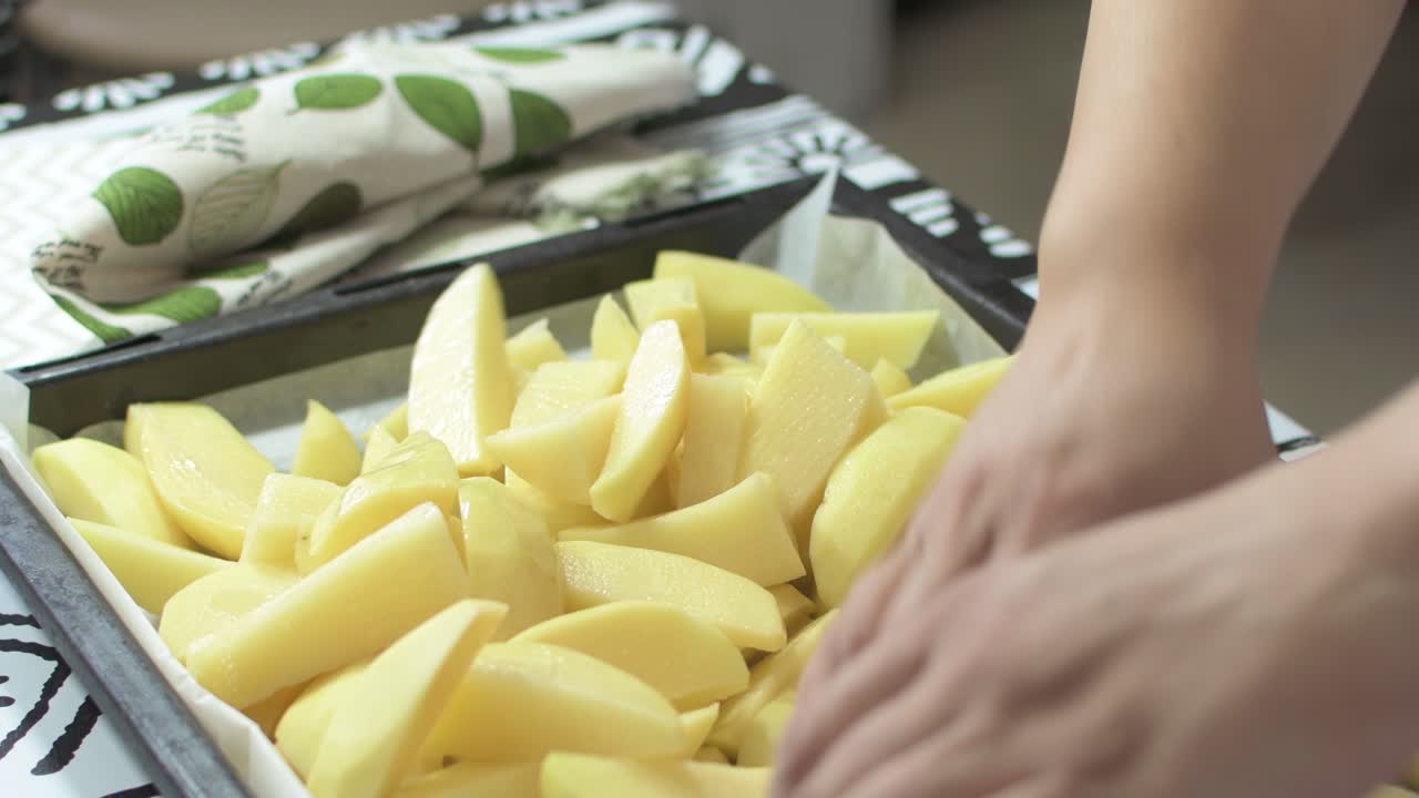 Lady's hands stirring potatoes so that they are impregnated with oil, to cook them in the oven.