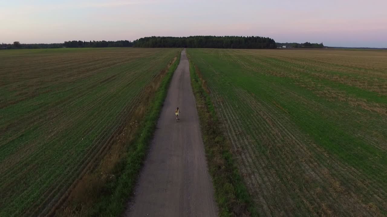 노란 드레스를 입은 어린 소녀가 저녁에 자갈길에서 자전거를 탄다