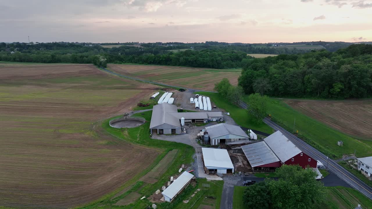 American Farmstead with house and barn in Pennsylvania. Aerial flyover shot. Cloudy sunrise in American countryside. Wide shot. hay bales covered with plastic foils.