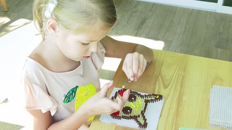 child creating pixel art with beads