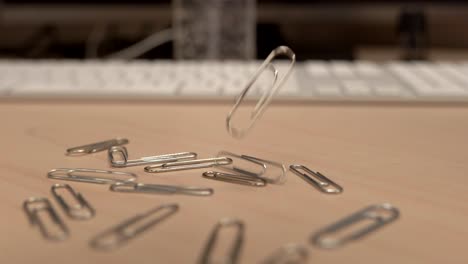 a hand full of paper clips slowly dropping onto an office desk in slow motion a little bit at a time