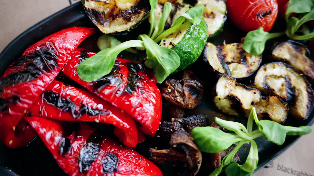 A black plate of grilled peppers, cherry tomatoes, zucchini, eggplant and mushrooms
