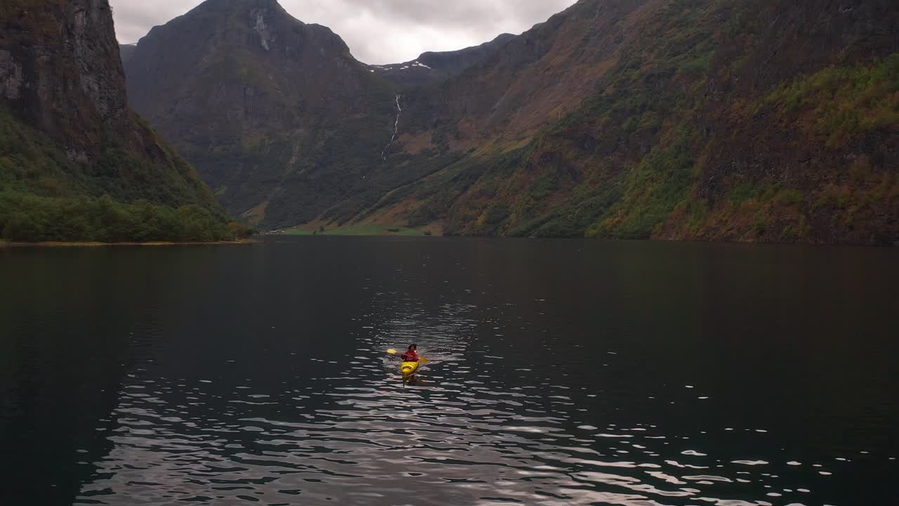 A person kayaking on a peaceful fjord surrounded by Norwegian mountains