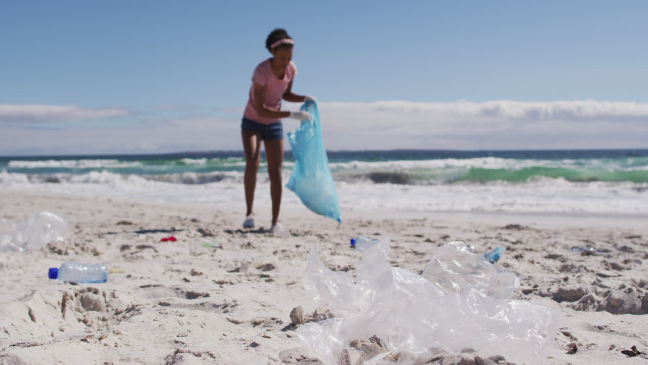 mujer afroamericana recogiendo desechos plásticos en la playa