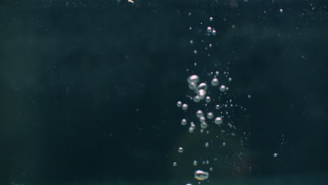 limón cayendo en el agua con burbujas en fondo oscuro.