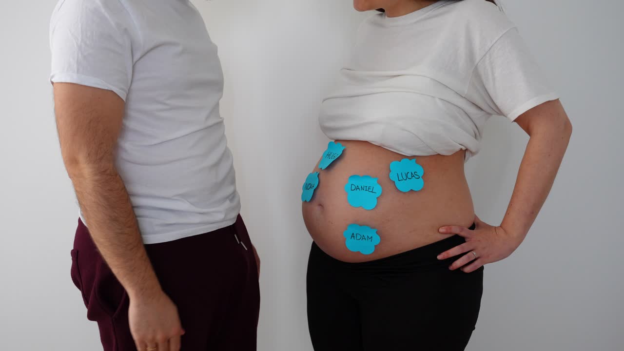 Male removing pink sticky notes with female names from the belly of his pregnant wife announcing it is a boy
