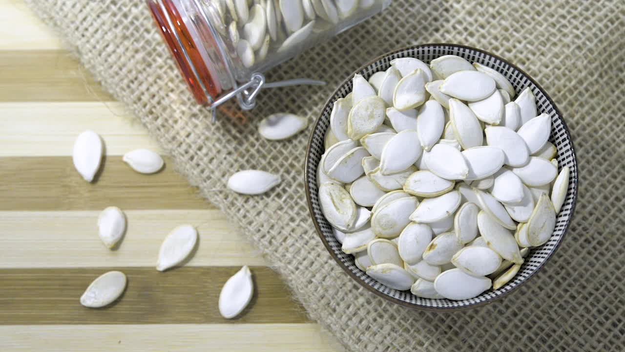 헤시안 천으로 줄무늬 테이블에 건포도 밤나무 혼합물로 채워진 유리병 세라믹 그릇을 통해 천천히 패닝 샷 위에서 아래로 보기