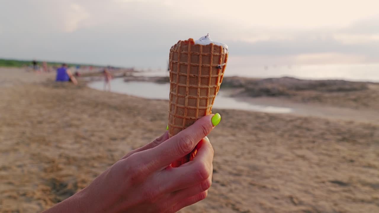 Close up of female hand holding ice cream on summer beach with sunset view