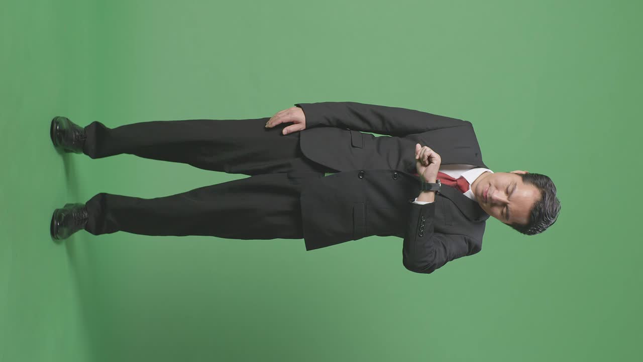 분노 한 아시아 사업가 의 몸 이 가득 차 있으며, 스튜디오 에서 녹색 스크린 에 서 있는 동안 휴대 전화 로 이야기 하고 있다