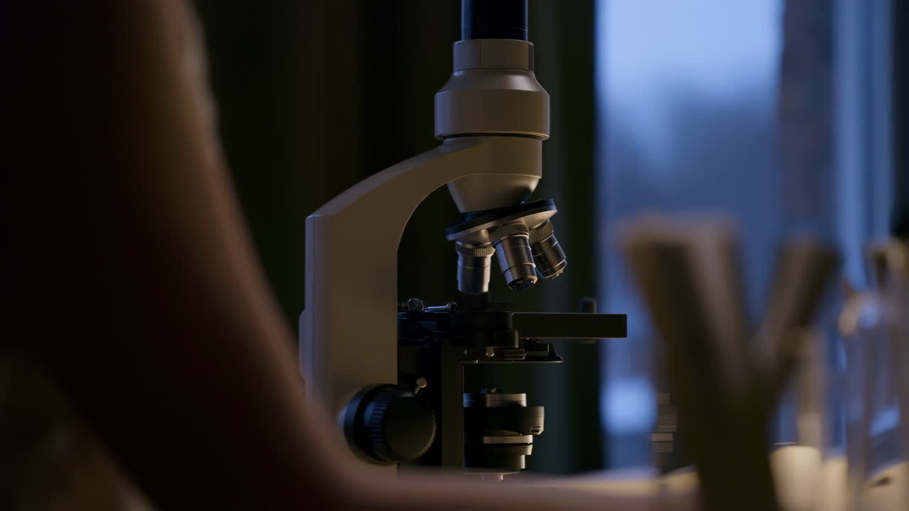 Close-up of a microscope in a laboratory setting with a person in the foreground