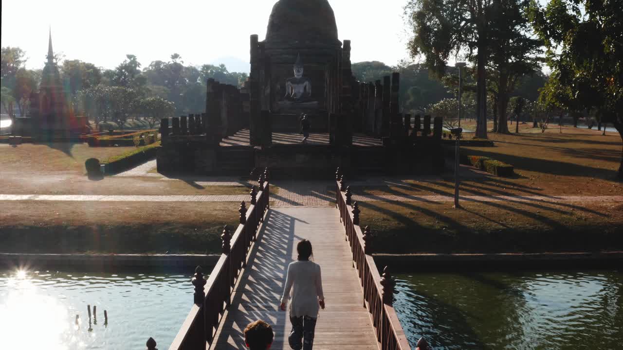 chica caminando por el puente hacia el templo de buda en el parque histórico de sukhothai, tailandia