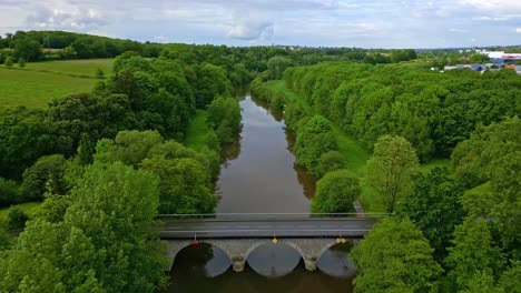 a serene river flowing through a lush green forest, with a classic stone bridge crossing it.