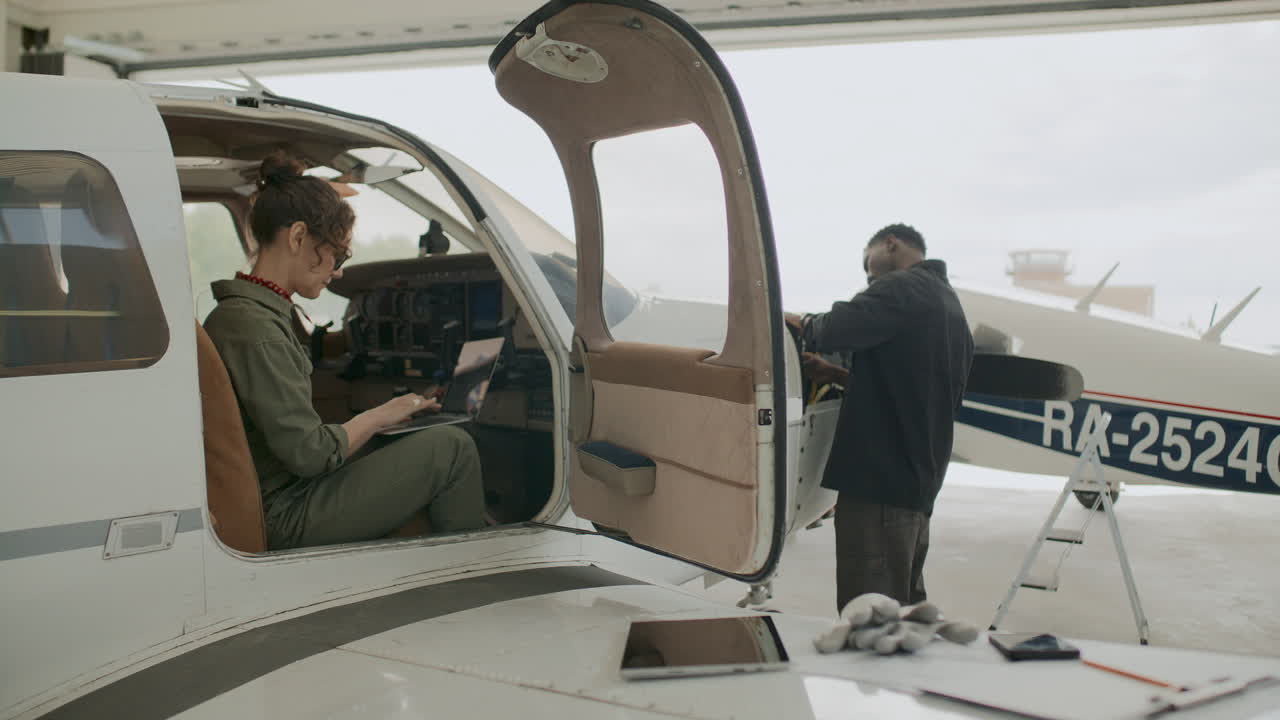Female Aviation Inspector Using Laptop and Checking on Technician in Hangar