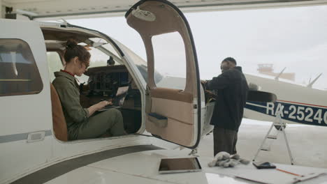 female aviation inspector using laptop and checking on technician in hangar