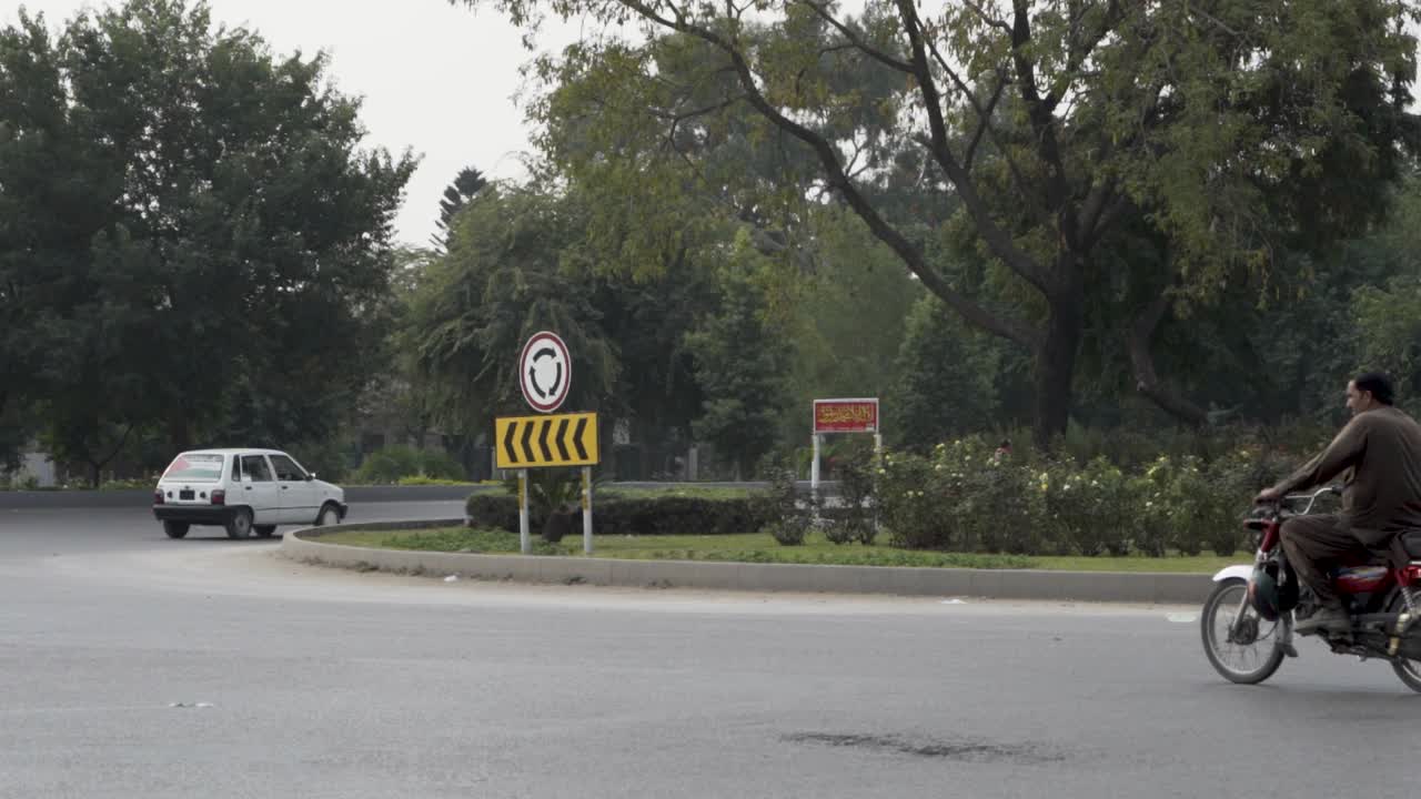 Slow-motion footage captures traffic moving around a roundabout with a visible sign.