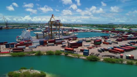 Shipping-container-port,-cranes-by-boat-docked,-blue-sky-sunny-day,-drone-aerial-orbit-Caribbean-island-of-Curacao