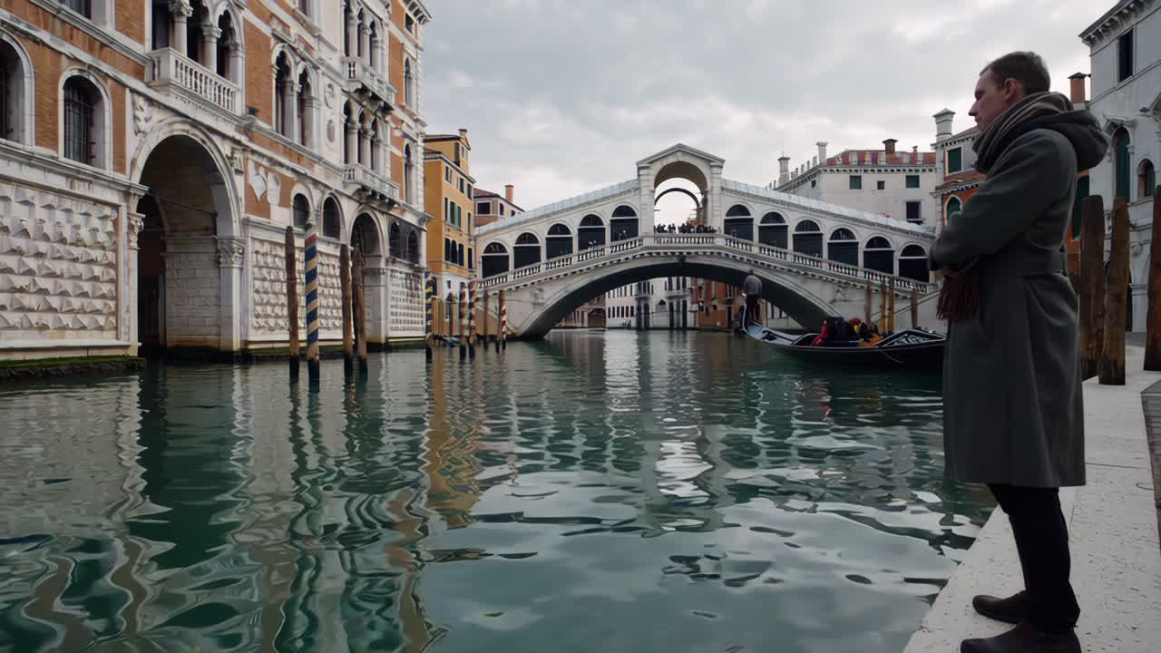 Mężczyzna stojący na brzegu kanału w Wenecji, patrzący na Most Rialto.