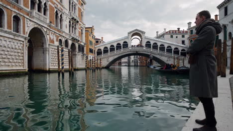 man standing on the bank of a venice canal, looking at the rialto bridge