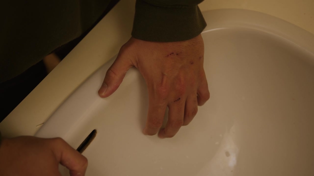 Close up shot over a man flexing his hands while putting then on a white basin inside a bathroom.