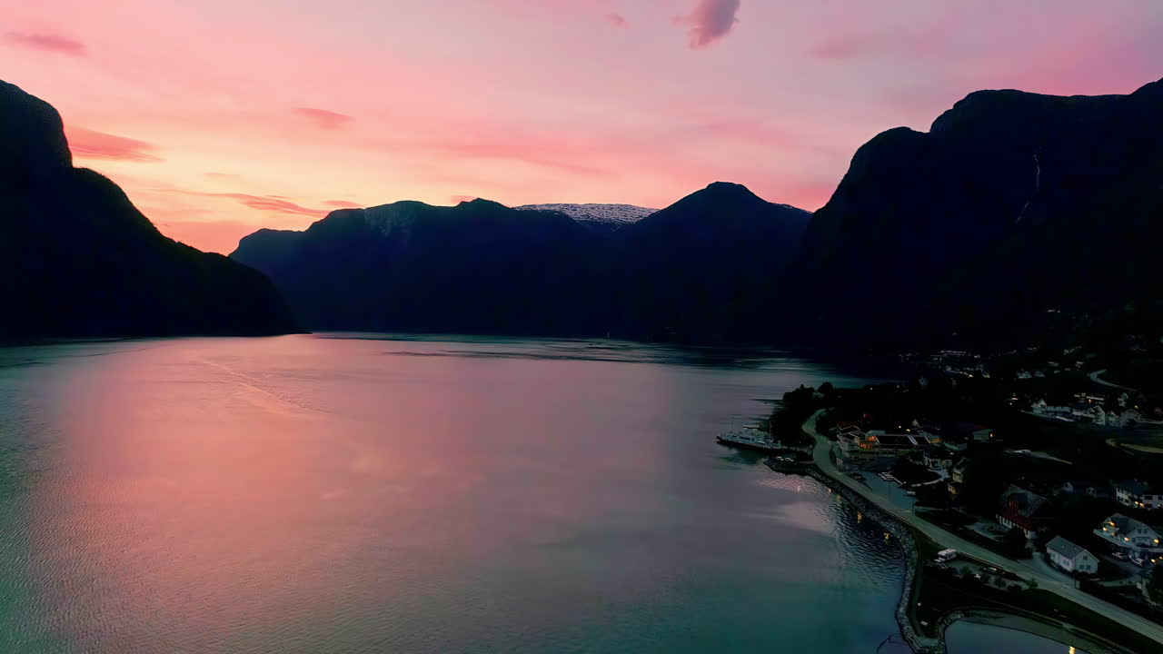 Stunning aerial shot of golden hour pink light that reflects in the lake and black silhouettes of the mountains in buhe background of a norwegian village