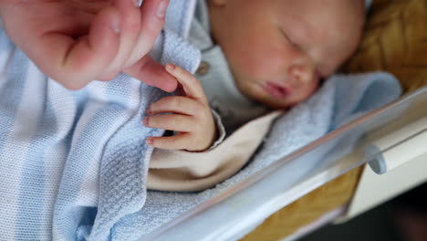 infant sleeping tight in a little crib. dad's hand touching cute tiny fingers of a newborn. close up.