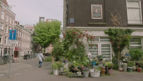 static shot of a typical amsterdam street with people walking next to a beautiful plant store on a spring day