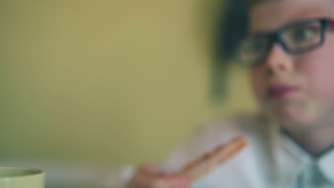 boy eats slice of pizza ans friend does home task at table