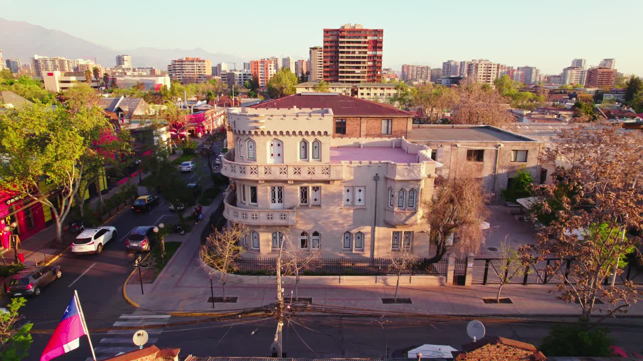 A bird's eye view dolly in the Sermini Palace or Castillo Los Jesuitas in a residential neighborhood of Providencia, Chilean flag waving at sunset