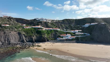 Aerial-view-of-white-villas-and-resorts-with-orange-rooftops-built-on-rugged-cliffs-along-a-beautiful-sunny-bay